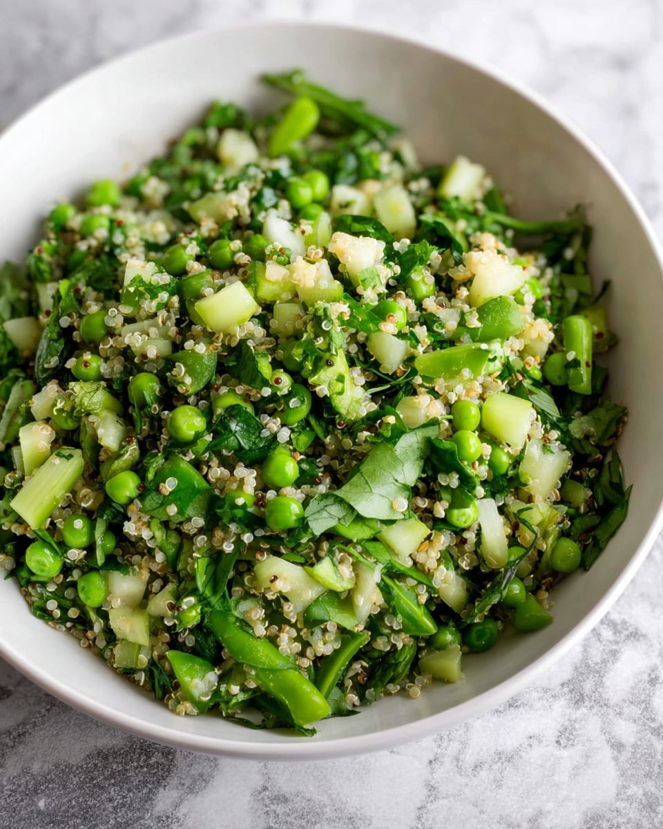 The image shows a white bowl filled with a fresh, mixed salad with no visible layers but a mix of various small pieces throughout. The salad contains green peas, light green celery, chopped green spinach leaves, and small white quinoa grains all evenly combined, creating a textured look with different shades of green and touches of white. The bowl is placed on a white marbled surface. photo taken with an iphone --ar 4:5 --v 7