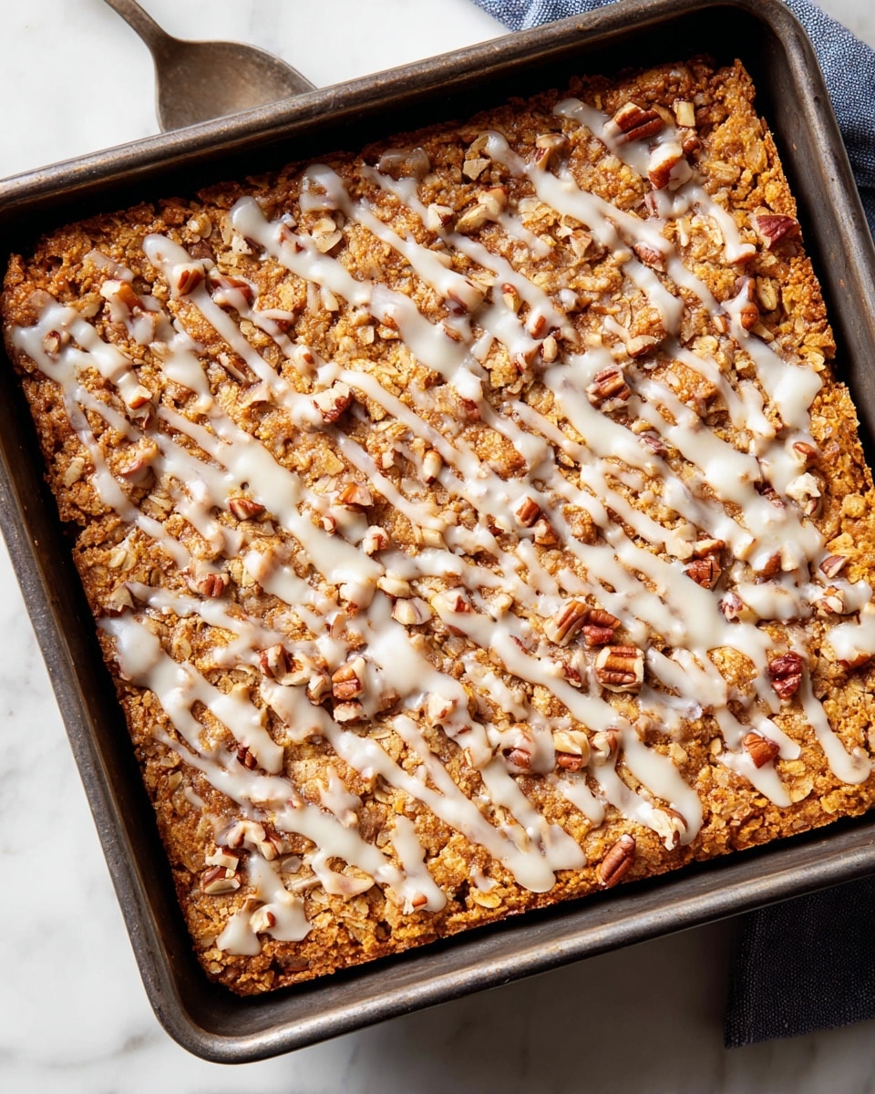 A square baked bar inside a dark metal pan sits on a white marbled surface, showing a single thick layer with a golden brown, rough, oat-like texture. A white icing is drizzled unevenly over the top, creating thin, curving lines that contrast with the warm orange-brown base. Small pieces of chopped pecans are scattered across the surface, adding extra texture and color variation with their light brown and off-white shades. Photo taken with an iphone --ar 4:5 --v 7