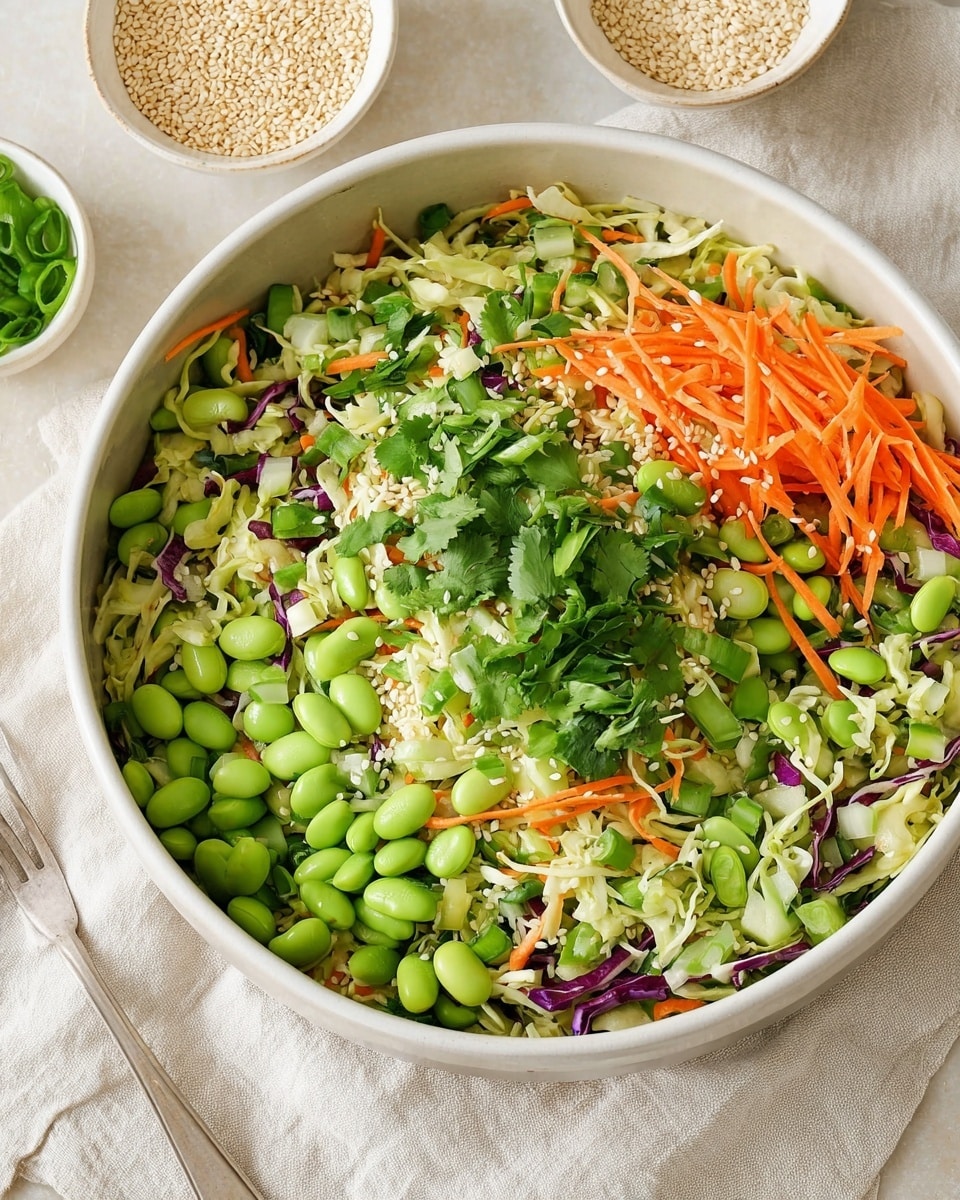 A white bowl is filled with a colorful salad featuring three main layers: the bottom layer has thin shredded light green cabbage, the middle layer contains thin orange carrot sticks and chopped light green cucumber pieces, and the top layer is bright green with shelled edamame beans and fresh chopped herbs like cilantro and green onions, all sprinkled with white sesame seeds. The bowl sits on a beige cloth on a white marbled surface, surrounded by scattered sesame seeds, a small white creamer with dark soy sauce, a wooden spoon filled with sesame seeds, a small white bowl with chopped green onions, and some loose cilantro leaves. A woman's hand holds silver forks resting in front of the bowl. Photo taken with an iphone --ar 4:5 --v 7
