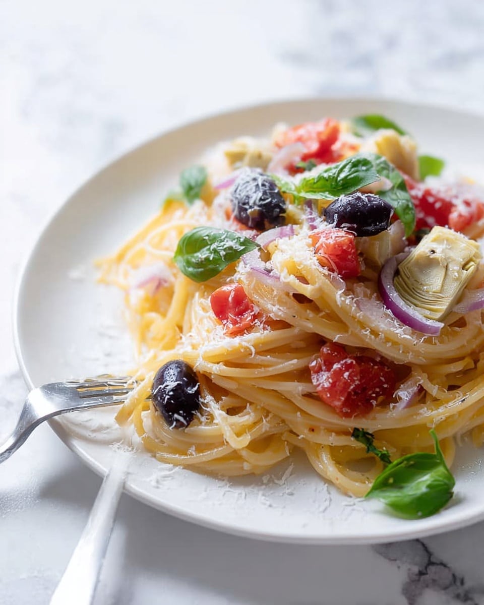 A white plate with a serving of spaghetti pasta arranged in loose circular piles forms the base layer, with a pale yellow color and smooth texture. On top, there are scattered chunks of red tomato pieces and small rings of translucent white and purple onion, adding bright red and light violet hues. Layered amid the pasta are whole black olives with a shiny, smooth surface and pale beige quartered artichoke hearts with a soft, fibrous texture. The dish is lightly dusted with fine white grated cheese and dotted with fresh green basil leaves and small sprigs of herbs, creating a varied texture and natural look. A silver fork rests on the plate's edge, partially holding some pasta strands. The background is a white marbled surface, contributing to a clean and fresh presentation. Photo taken with an iphone --ar 4:5 --v 7
