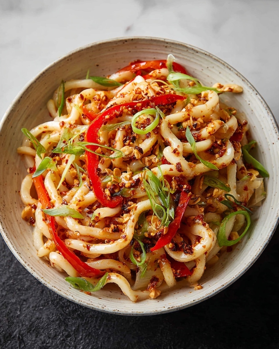 A black bowl filled with thick, pale beige noodles coated in a light sauce, lifted by chopsticks from above. Mixed in and under the noodles are small golden-brown crispy tofu cubes, thin slices of bright red bell pepper, and scattered green onion strands. The noodles have a slight shine and tiny bits of chili flakes. The bowl is set on a white marbled texture. photo taken with an iphone --ar 4:5 --v 7