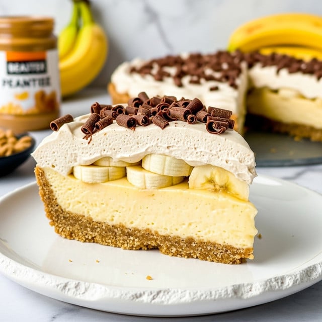 A slice of banana cream pie is shown on a white plate with a rough edge. At the bottom is a thick, golden brown crumb crust. Next is a smooth, glossy, pale yellow banana filling. Above the filling are slices of yellow banana. On top is a thick layer of creamy, light tan whipped topping, sprinkled with shiny dark brown chocolate curls. The background features a white marbled texture with blurred yellow bananas and a jar of peanut butter. photo taken with an iphone --ar 4:5 --v 7