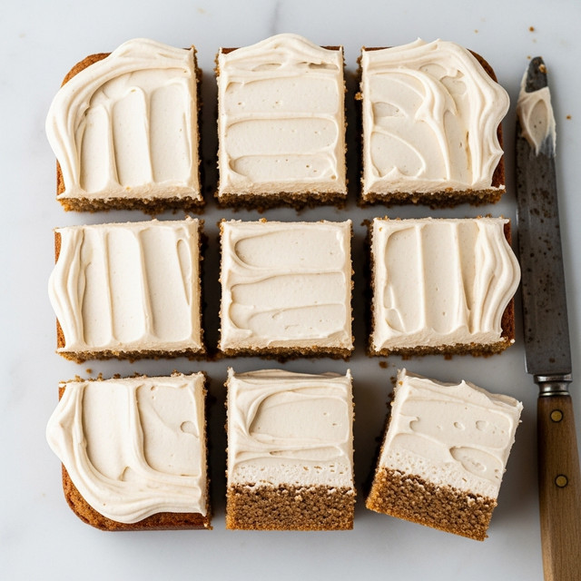 A square cake cut into nine pieces is shown from above, each piece having one thick layer of brown cake at the bottom and a thick, smooth layer of light beige frosting on top with soft spreads and swirling textures. The cake rests on a white marbled texture surface, with a metal spatula partly visible at the bottom left corner. The frosting is creamy and slightly speckled, covering the entire top surface evenly with a few artistic swirls. photo taken with an iphone --ar 4:5 --v 7
