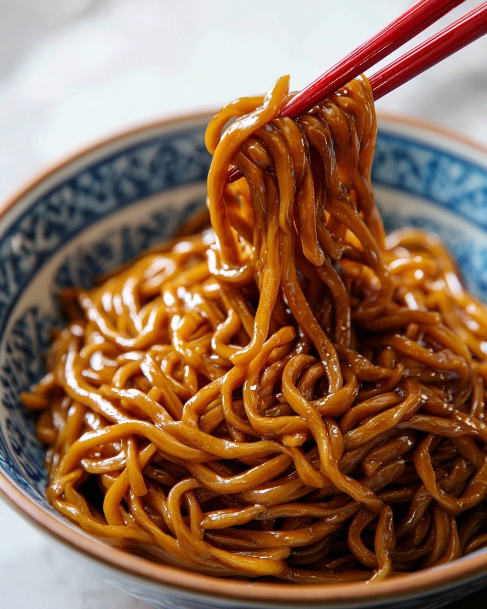 The image shows a close-up of a bowl filled with shiny, thick strands of noodles coated in a rich, brown sauce. The noodles have a smooth, glossy texture and a slightly twisted shape, gathered together by a pair of red chopsticks lifting them from the bowl. The bowl itself is white with blue patterns inside, creating a nice contrast with the dark noodles. The background features a white marbled texture that adds a clean and bright look to the scene. photo taken with an iphone --ar 4:5 --v 7