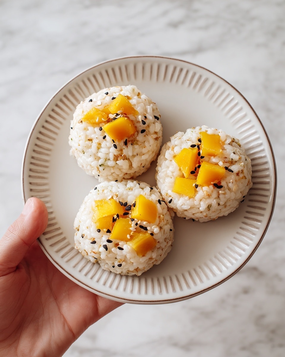 Three round rice cakes sit closely on a white plate with a subtle dotted rim. Each cake has a pale cream color with a slightly grainy texture, embedded with chunks of bright yellow mango pieces on top. Scattered around the mango are tiny black and white sesame seeds adding contrast and small specks of texture. A woman's hand holds the plate from the bottom left corner, set against a white marbled textured background. photo taken with an iphone --ar 4:5 --v 7