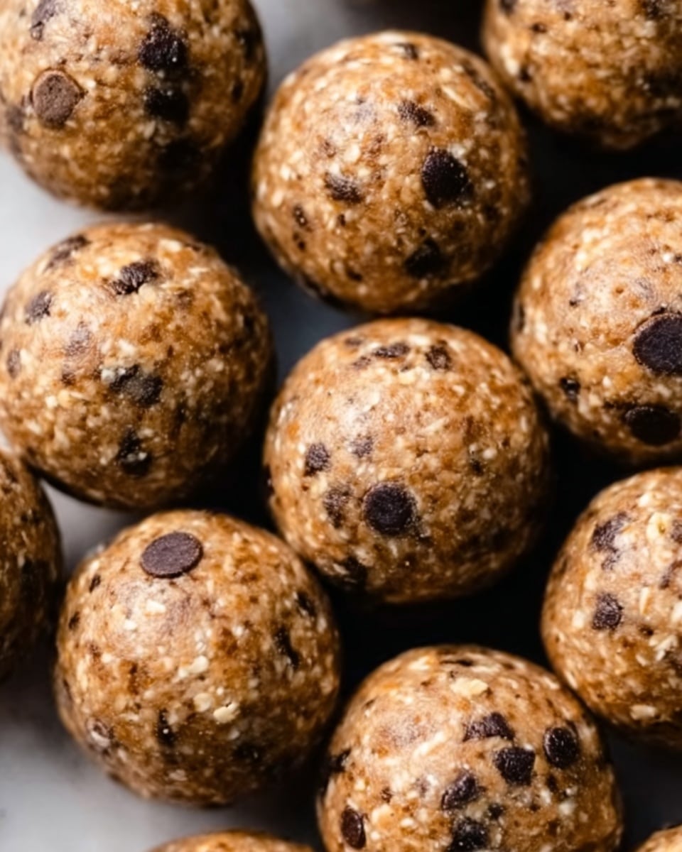 The image shows many round energy balls packed closely together, each with a light brown color mixed with small dark brown chocolate chips scattered throughout. The texture looks soft and slightly bumpy, with visible oats and seeds inside. The surface is shiny and gives a fresh, healthy snack feeling. photo taken with an iphone --ar 4:5 --v 7
