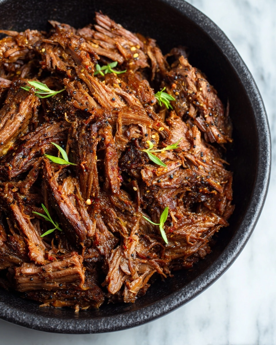 The image shows a close-up of shredded dark brown beef with a moist, tender texture piled in a black dish. The beef is seasoned with visible specks of black pepper and coarsely ground spices. Small green sprigs of fresh herbs are scattered on top, adding a touch of color. The beef fibers are well-defined, showing the meat's softness and juiciness, with the meat layers overlapping naturally inside the dish. The dish rests on a white marbled surface. photo taken with an iphone --ar 4:5 --v 7