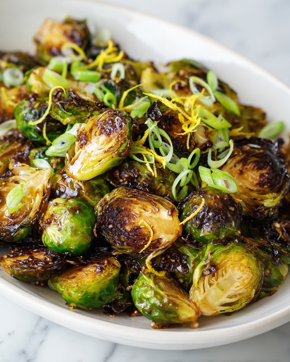 The image shows roasted Brussels sprouts with a rich caramelized brown color on the outer leaves, clustered closely together. The sprouts are cut in halves or quarters, showing a soft, golden-yellow inside with crispy, dark green and brown edges. They are garnished on top with bright green sliced scallions and finely grated yellow lemon zest, adding fresh color accents. The dish sits on a white plate placed on a white marbled surface, with the Brussels sprouts appearing shiny and coated in a glaze that hints at a honey balsamic dressing. Photo taken with an iphone --ar 4:5 --v 7