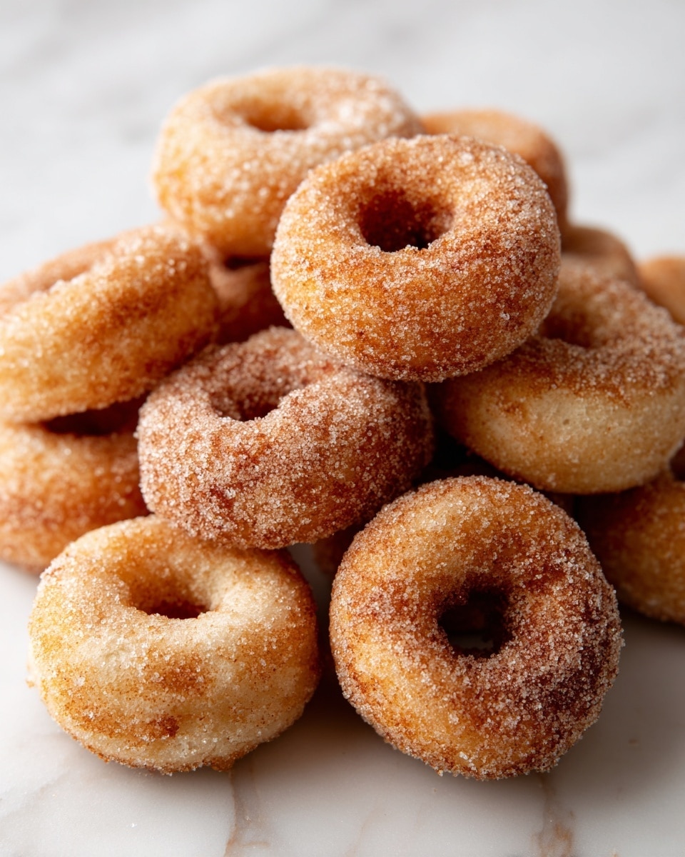 A group of small, round mini donuts with a golden-brown color are spread out over a white marbled surface. Each donut is evenly coated with fine white sugar, giving them a slightly sparkly look. The donuts have a soft texture with a small hole in the center of most, while some look slightly puffier without a visible hole. The light creates gentle highlights and shadows on the donuts, showing their fluffy and slightly crispy exterior. photo taken with an iphone --ar 4:5 --v 7