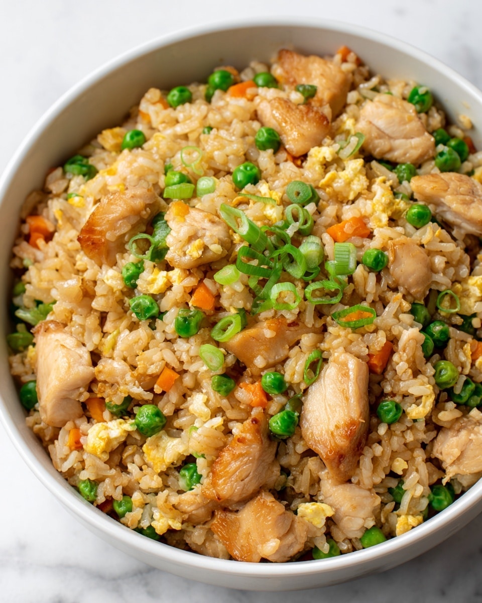 The image shows a bowl of fried rice with three main layers: the base layer is cooked rice with a light brown color, mixed evenly throughout; the second layer has bright orange carrot chunks and green peas scattered on top and within the rice; the third layer consists of light tan chicken pieces placed on top and mixed inside, giving texture and bulk to the dish. Small bits of green onions are sprinkled across the top, adding a fresh, green touch. The bowl is white, and it sits on a white marbled surface. photo taken with an iphone --ar 4:5 --v 7
