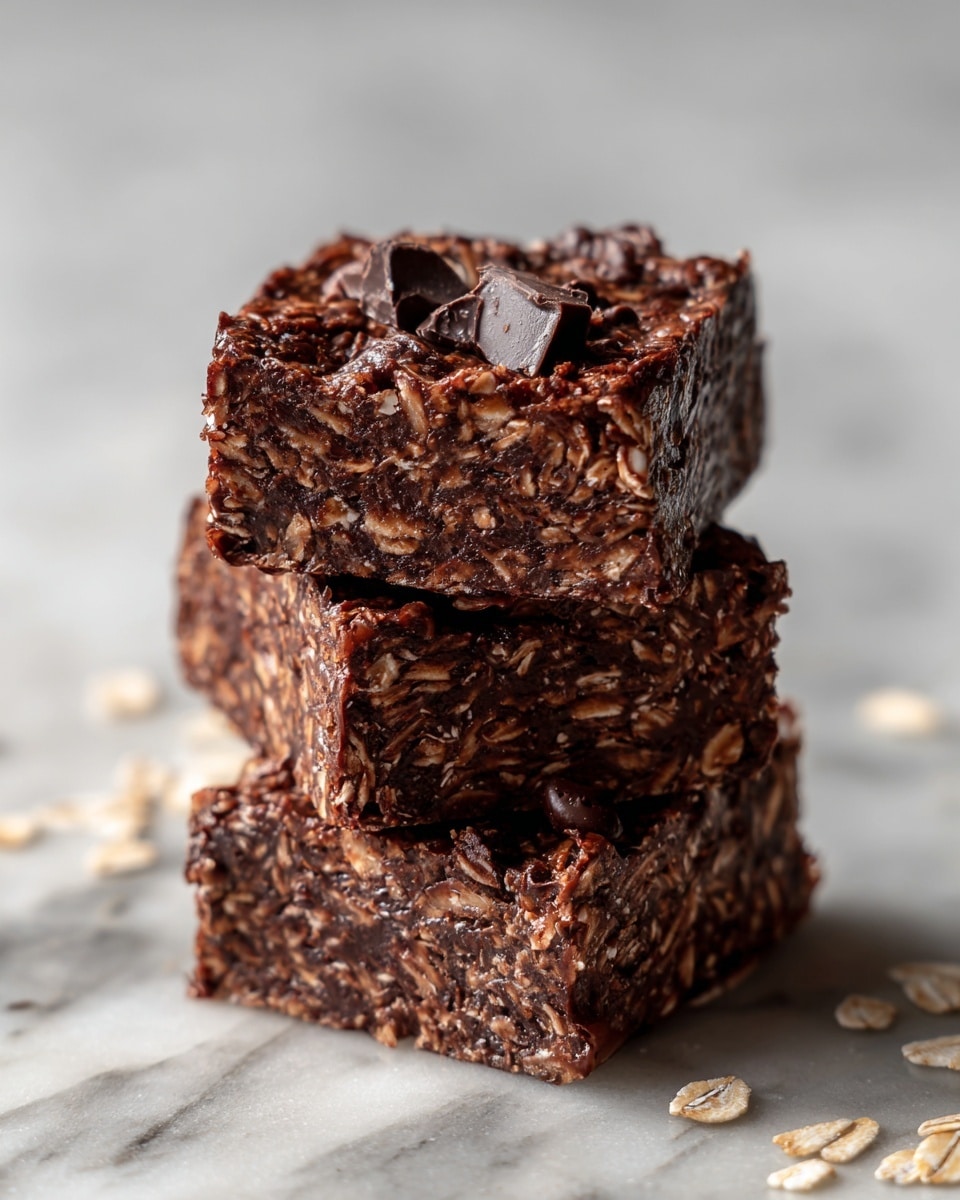 The image shows three thick, square chocolate oat bars stacked on top of each other. Each bar has a rich, dark brown color with visible bits of oats and chocolate chips mixed evenly throughout. The texture looks dense yet crumbly, with a slightly glossy surface that hints at melted chocolate. The background has a white marbled texture with scattered small oat flakes and chocolate crumbs around the bars, adding a rustic feel. The lighting softens the edges, making the bars look moist and inviting. Photo taken with an iphone --ar 4:5 --v 7