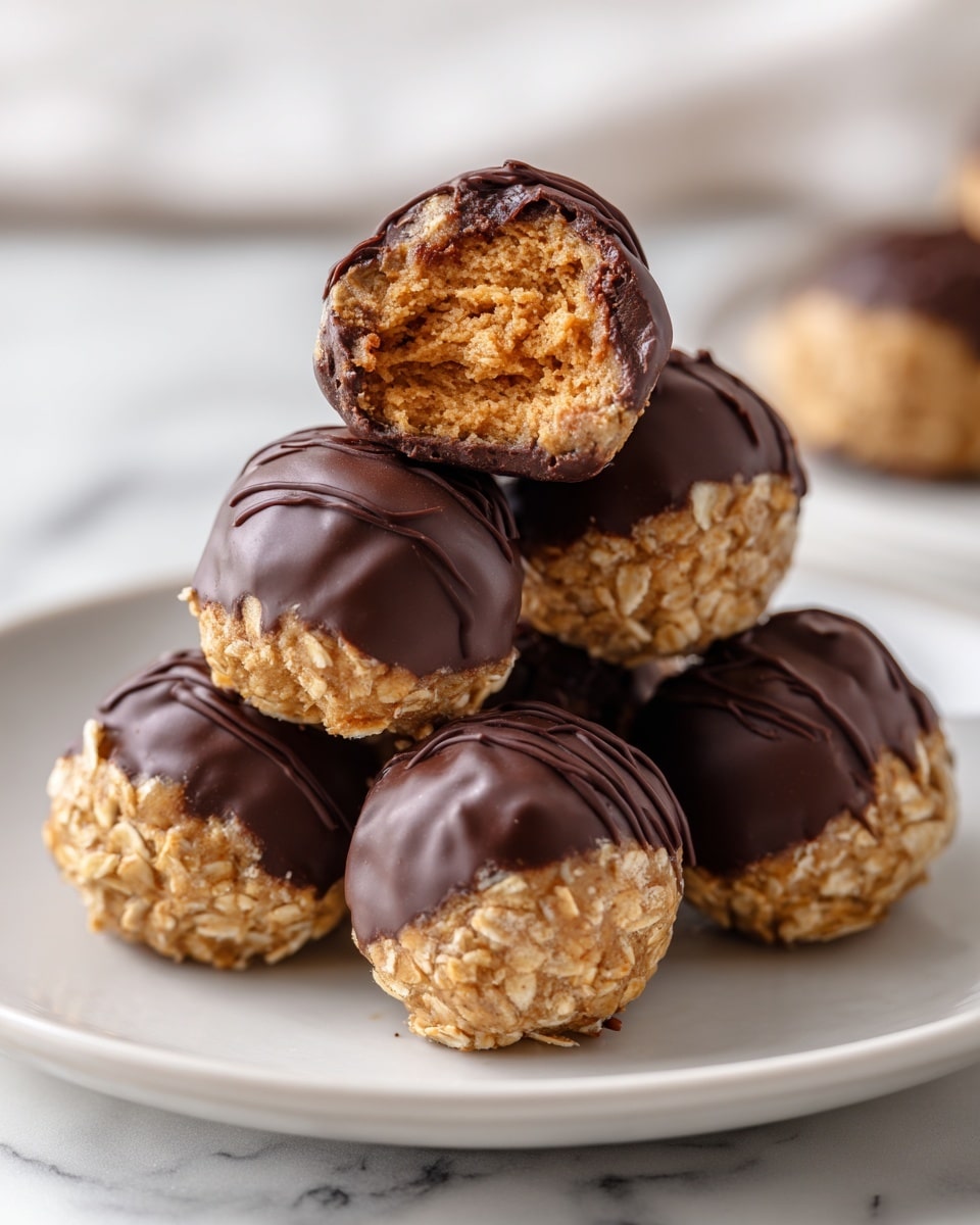A pile of round energy balls on a white plate placed on a white marbled surface, each ball has two layers: an inner layer showing a light brown, oat-filled, textured mixture, and an outer shell of smooth, glossy dark chocolate partially coating the top and sides, with one ball at the top having a bite taken out showing the soft, crumbly inside. photo taken with an iphone --ar 4:5 --v 7