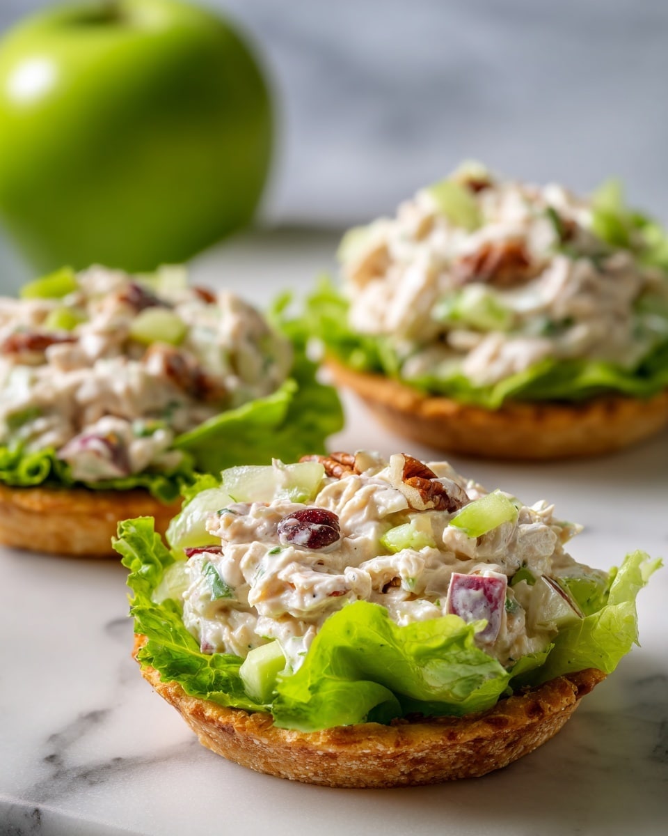 Small round slices of bright orange sweet potato form the base layer, topped with a thick mound of creamy salad mixture containing white, pale green, small dark red, and crunchy brown bits. This salad sits on a fresh green bed of leafy lettuce. The white plate below rests on a white marbled surface, with glimpses of green apples and pink flower petals blurred in the background. The scene is brightly lit, showing the textures of the creamy salad, crisp lettuce, and smooth sweet potato clearly. Photo taken with an iphone --ar 4:5 --v 7