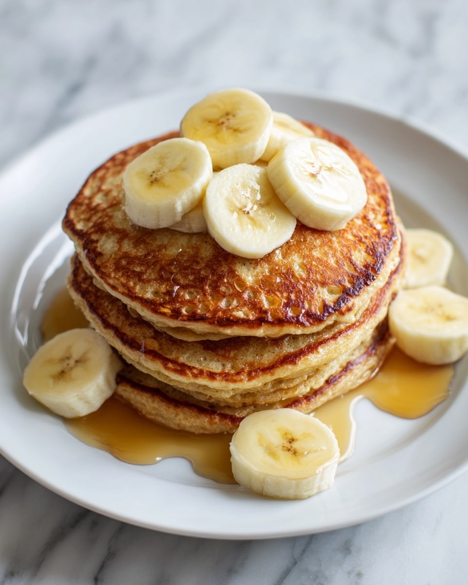 A stack of four golden-brown pancakes sits in the middle of a white plate, each pancake thick with a slightly bubbly texture on top. On the top pancake, there are several slices of light yellow banana arranged in a small pile. Some banana slices also rest around the bottom pancake on the plate. Light amber syrup is drizzled generously over the pancakes and pools slightly on the plate, creating a glossy, sticky look. The whole scene is set on a white marbled surface, adding a clean and simple background. Photo taken with an iphone --ar 4:5 --v 7