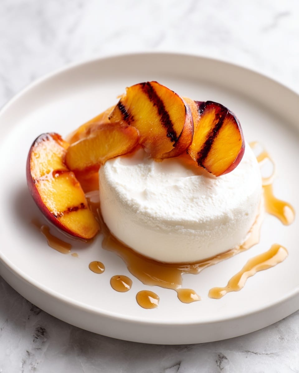 A white plate holds a smooth, thick white cream spread in a round shape at the center. On top sits half of a grilled peach with dark brown grill marks and a soft orange color, angled slightly to show the inside and outside. Next to this half is a small wedge of peach with a similar orange tone. Light brown syrup is drizzled in small lines around the cream on the plate. The background is a white marbled texture. Photo taken with an iphone --ar 4:5 --v 7