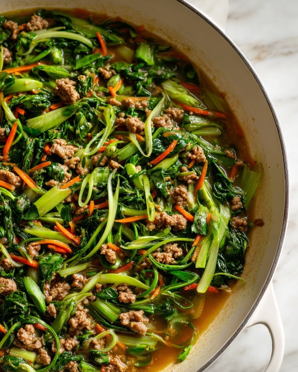 The dish is shown inside a white cooking pan with a slightly worn rim on a white marbled surface. It has three main layers: the base is a light brown, slightly oily sauce. On top of this, there are uneven chunks of cooked ground meat, tan to brown in color with a rough texture. Scattered throughout are chunks and strips of bright and dark green leafy vegetables with a fresh, slightly wilted look, mixed with thin slices of orange carrots adding pops of color. The ingredients are mixed together, giving the dish a moist and saucy appearance overall. photo taken with an iphone --ar 4:5 --v 7