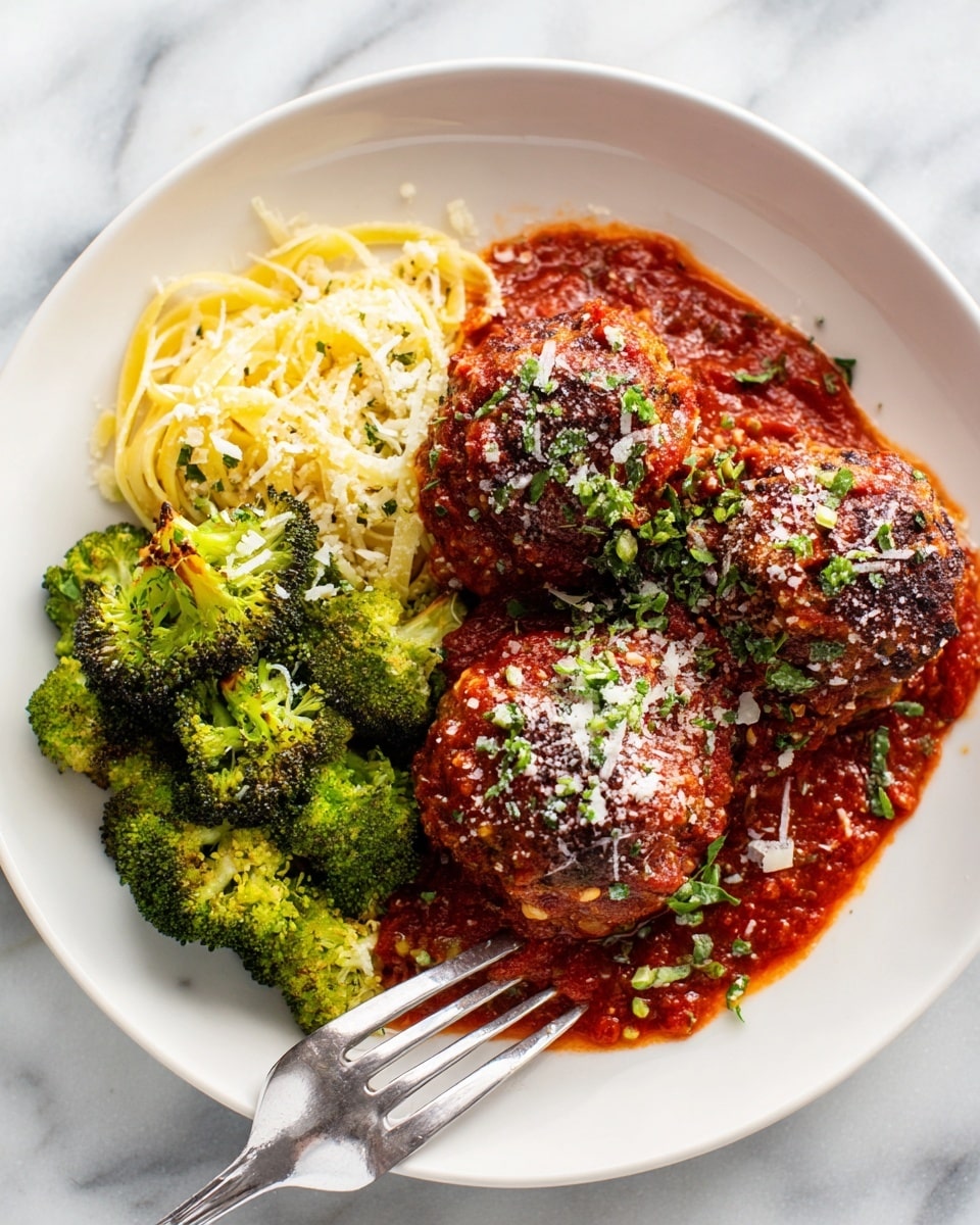A white plate holds three browned meatballs covered with a thick layer of bright red marinara sauce and sprinkled with finely grated white cheese and small green herb pieces on top. Next to the meatballs is a serving of light yellow spaghetti noodles arranged in loose loops. To the side, there are several green broccoli florets with charred, crisp edges showing a mix of dark green and brown colors. A silver fork rests partially under one meatball, all placed on a white marbled surface. Photo taken with an iphone --ar 4:5 --v 7