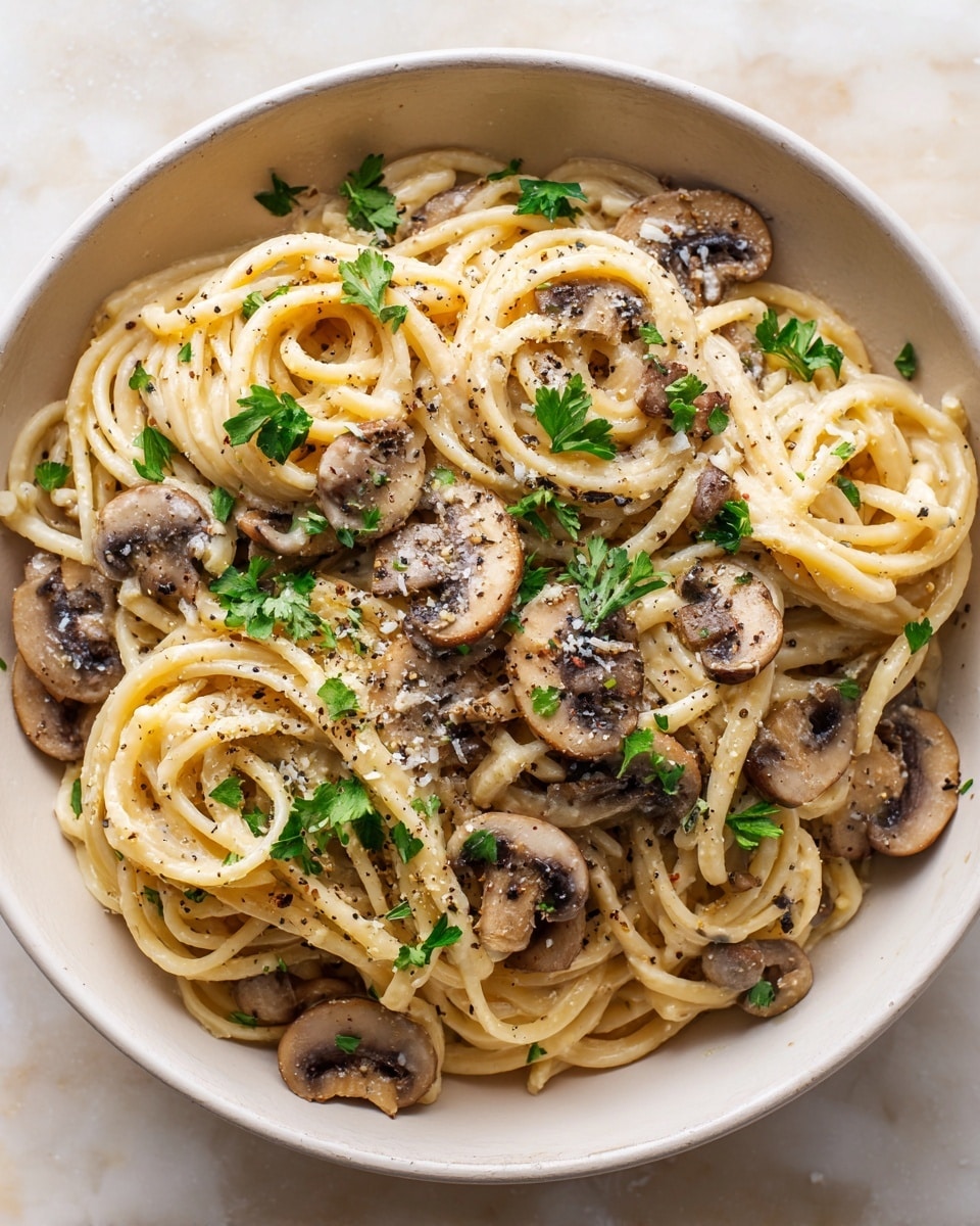 A white pan filled with creamy light brown pasta noodles mixed evenly with sliced brown mushrooms, topped with scattered fresh green parsley leaves and a sprinkle of black pepper and herbs, all sitting on a white marbled surface. The noodles have a smooth, slightly glossy texture and are arranged in loose, overlapping loops with mushroom slices spread throughout, giving a mix of soft and firm textures. Photo taken with an iphone --ar 4:5 --v 7
