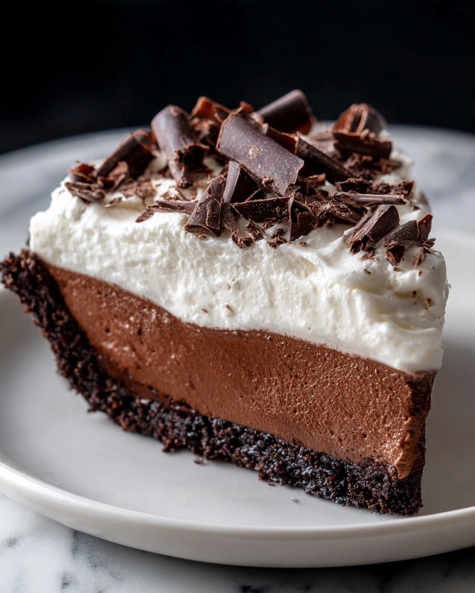 A slice of rich chocolate pie with three distinct layers sits on a white plate on a white marbled surface. The bottom layer is a dark, crumbly chocolate crust, followed by a smooth, dense chocolate filling in the middle that has a glossy texture. The top layer is a thick, fluffy white cream, decorated with several large, dark chocolate curls that curl and twist on top, creating height and texture. The contrast of the dark chocolate and white cream is clear and inviting, with the chocolate curls adding an elegant, decorative touch. photo taken with an iphone --ar 4:5 --v 7